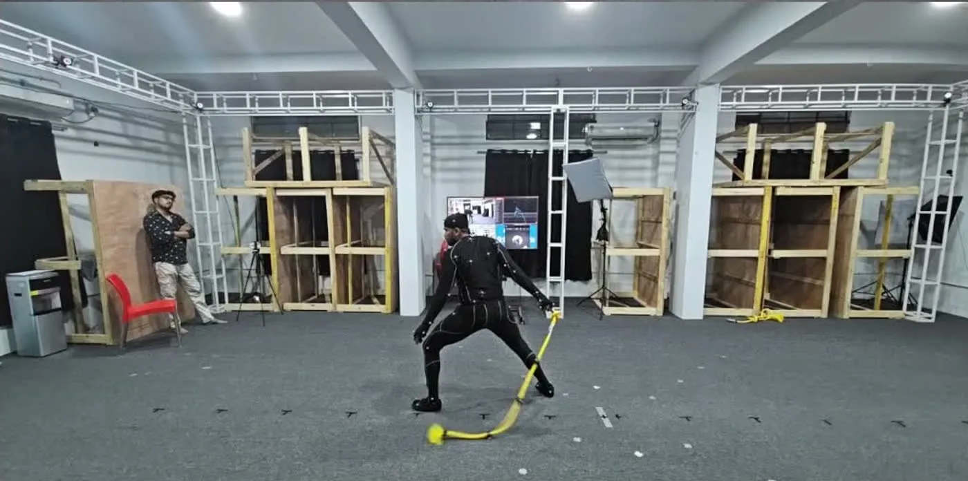 A performer swings a tracked prop inside the capture volume, cameras on the truss above